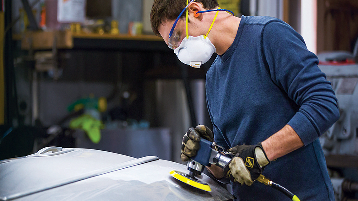 man using air sander on automobile door in shop